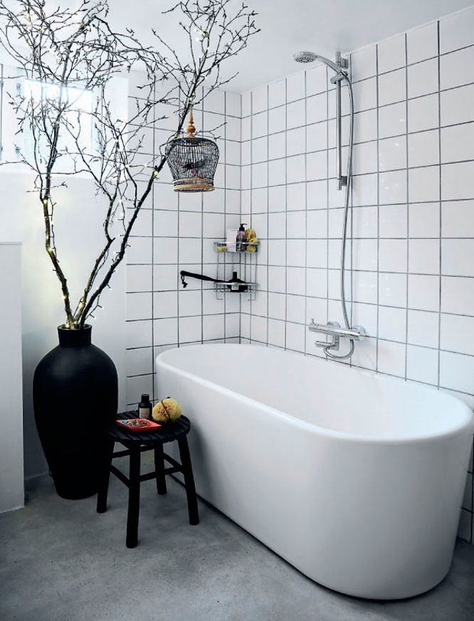 Badeværelse med stort badekar og højt træ med lysekæde.