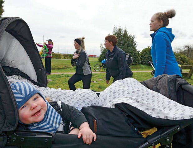Dreng ligger i barnevogn mens mødre dyrker efterfødselstræning