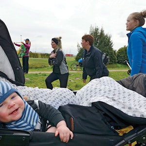 Dreng ligger i barnevogn mens mødre dyrker efterfødselstræning